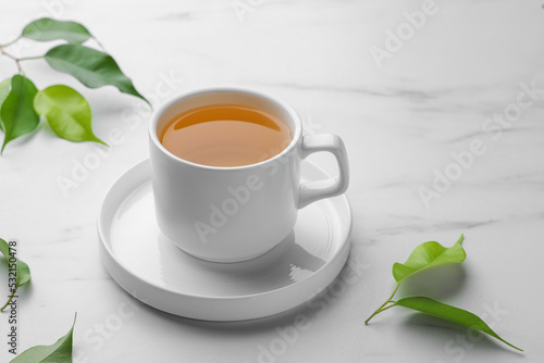 Green tea in cup with saucer and leaves on white marble table
