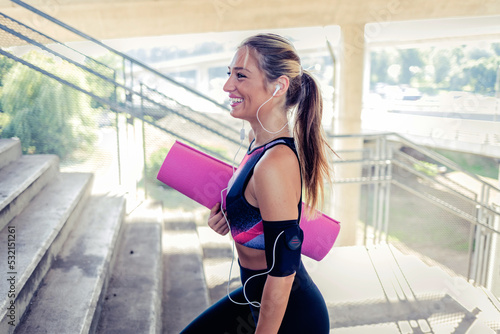 Cheerful young woman holding rolled up exercise mat. Fit, healthy and sporty woman in sportswear. Happy beautiful young woman with a yoga mat.