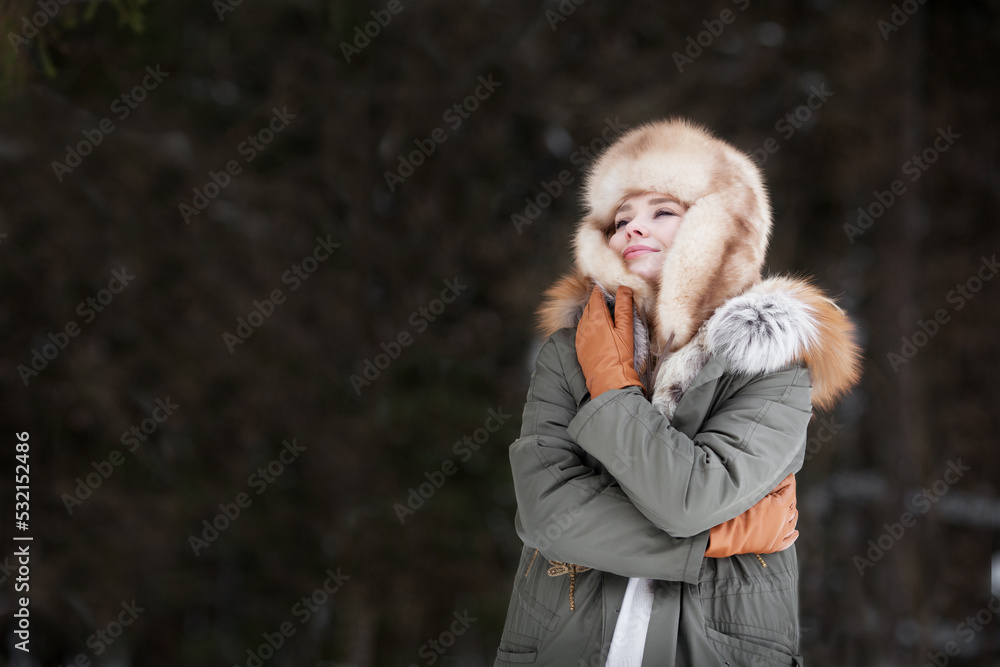 Woman wrap and hug herself on dark background, wearing winter jacket, fur ear flaps hat and leather glove. Cozy portrait Woman wrap and hug herself on dark background, wearing winter jacket, fur ear flaps hat and leather glove. Cozy portrait