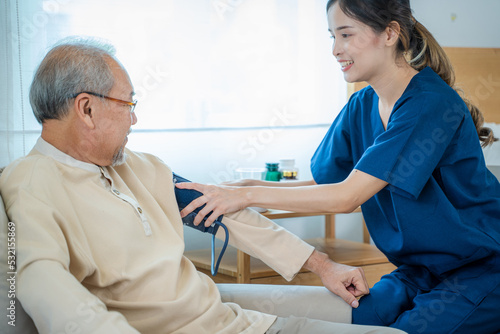 Happy nurse measuring blood pressure of a senior man in bedroom in a nursing home.