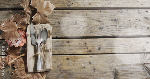 Image of light spots over cutlery and leaves on wooden background