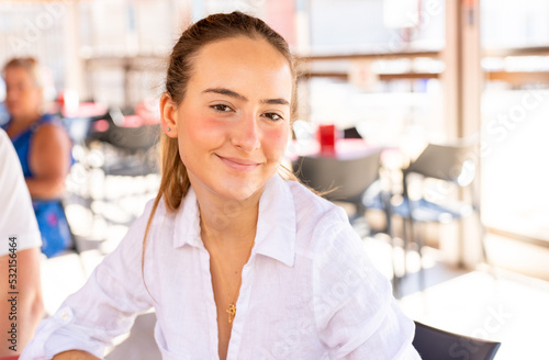 beautiful young woman wearing casual shirt sits at a table in a summer cafe.