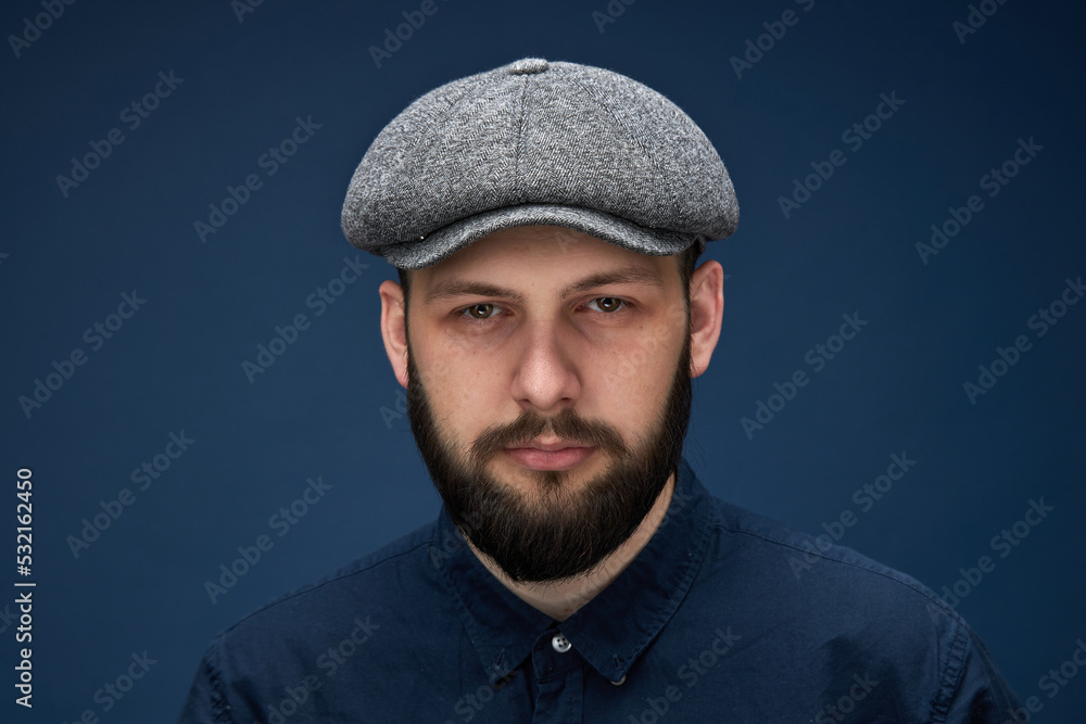 a man in a shirt with a beard and a cap on a dark blue background. a man in a shirt with a beard and a cap on a dark blue background.