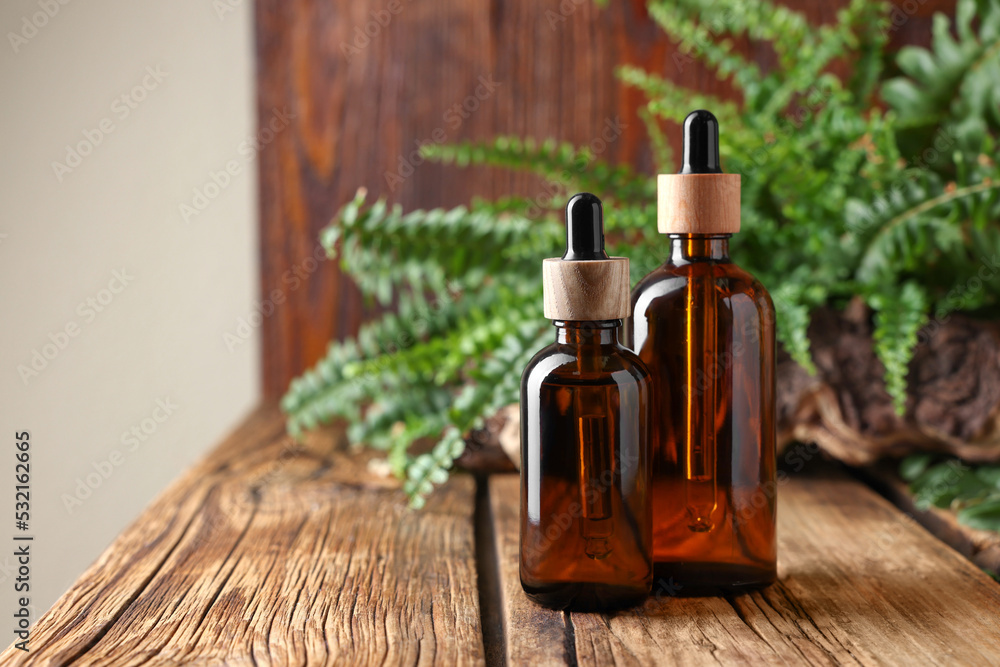 Glass bottles of essential oil on wooden table, space for text Glass bottles of essential oil on wooden table, space for text