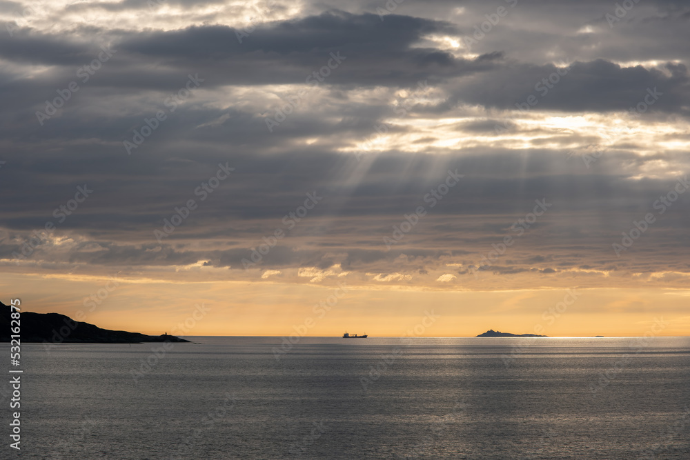 Wonderful landscapes in Norway. Vestland. Beautiful scenery of a cargo boat in the calm sea at the sunset in a cloudy day with sunrays through the clouds. Yellow sky. Selective focus
