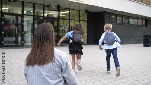 Mom takes the kids to school. The woman waves goodbye, the children run around the school yard.
