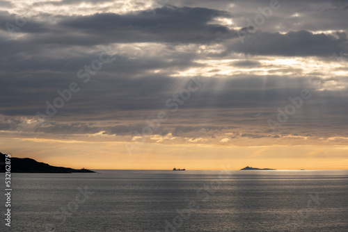 Wonderful landscapes in Norway. Vestland. Beautiful scenery of a cargo boat in the calm sea at the sunset in a cloudy day with sunrays through the clouds. Yellow sky. Selective focus © Maurizio