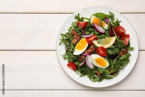 Delicious salad with boiled eggs, vegetables and bacon on white wooden table, top view. Space for text