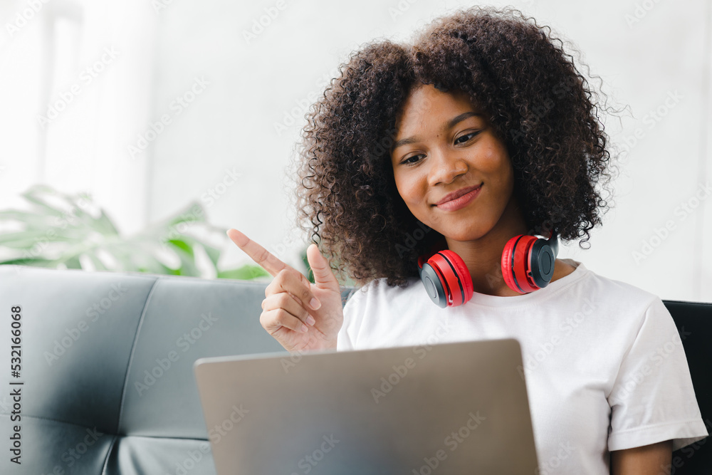 An American woman sits on a sofa on a laptop, video calls with friends, spends her weekend on social media, watches movies and listens to music at home. Holiday concept. An American woman sits on a sofa on a laptop, video calls with friends, spends her weekend on social media, watches movies and listens to music at home. Holiday concept.