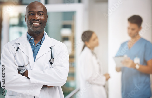 Doctor  healthcare and medicine with a man surgeon standing arms crossed in the hospital with his team in the background. Trust  insurance and care with a male health professional working in a clinic