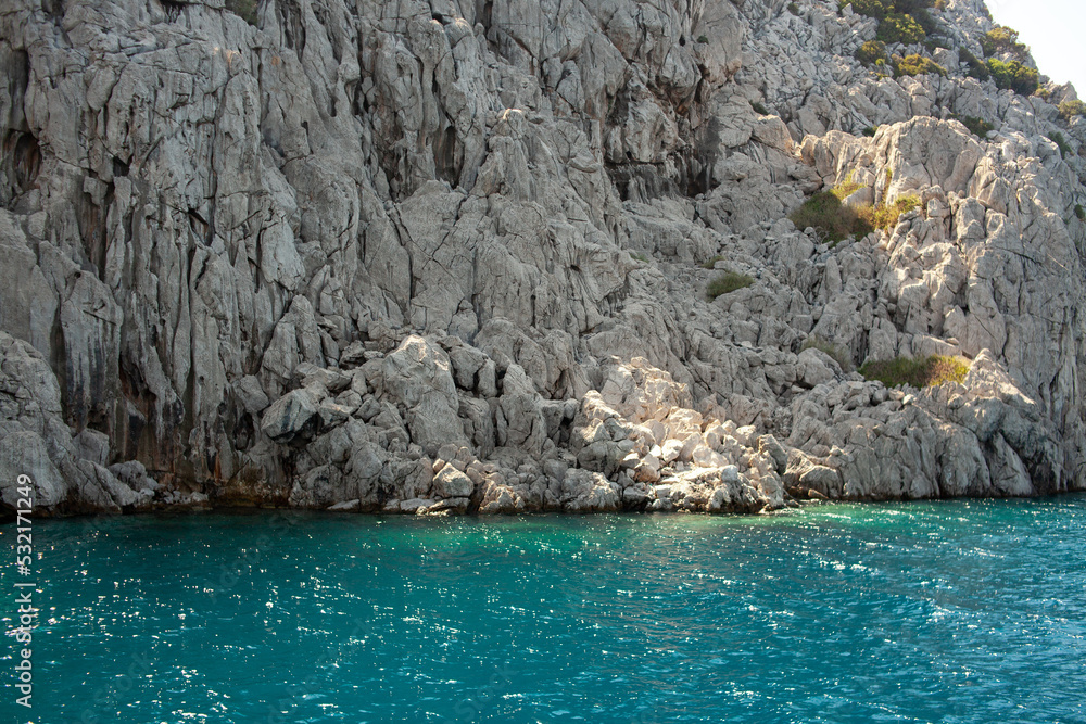 Aegean sea rocky shores with turquoise water. Lava stones and rocks. View from sea. Rock reflection in blue water sea.