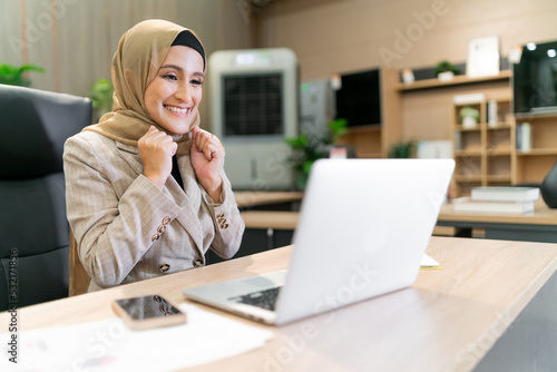 happy business muslim hijab woman work. islam woman pointing at laptop screen while having an online group meeting. success cheerful adult beautiful arabic person sitting touch screen consult people