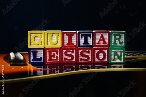 Word or phrase Guitar Lesson made with letter cubes, standing on guitar.