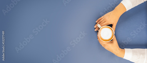 Cafe latte, top view photo of woman hands holding cafe latte. Menu, banner, poster concept idea with copy space. Isolated on dark blue background. Latte art design or hot cappuccino with milk.