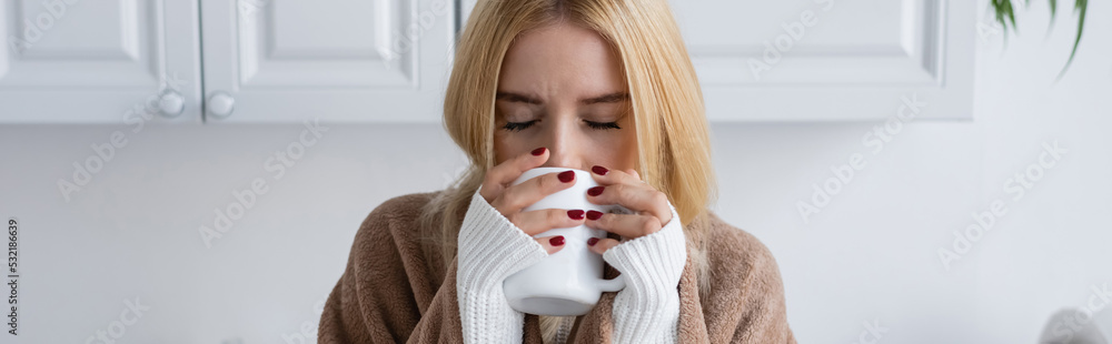 young blonde woman in sweater and blanket drinking tea from cup, banner. young blonde woman in sweater and blanket drinking tea from cup, banner.