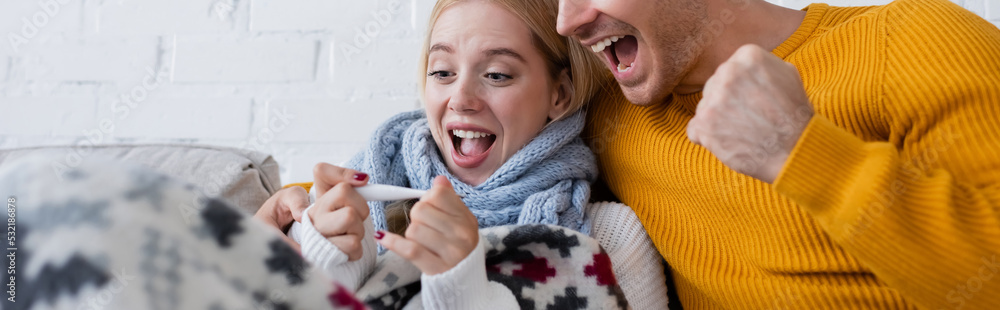 excited man and sick blonde woman looking at digital thermometer, banner. excited man and sick blonde woman looking at digital thermometer, banner.