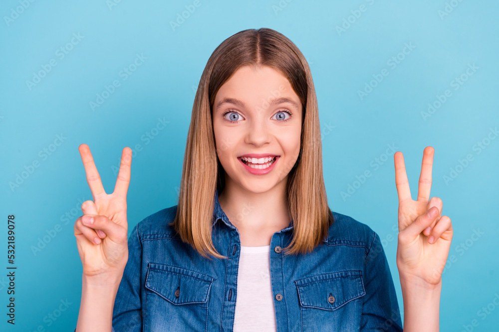 Photo of cool little blond girl show v-sign wear jeans shirt isolated on blue color background Photo of cool little blond girl show v-sign wear jeans shirt isolated on blue color background