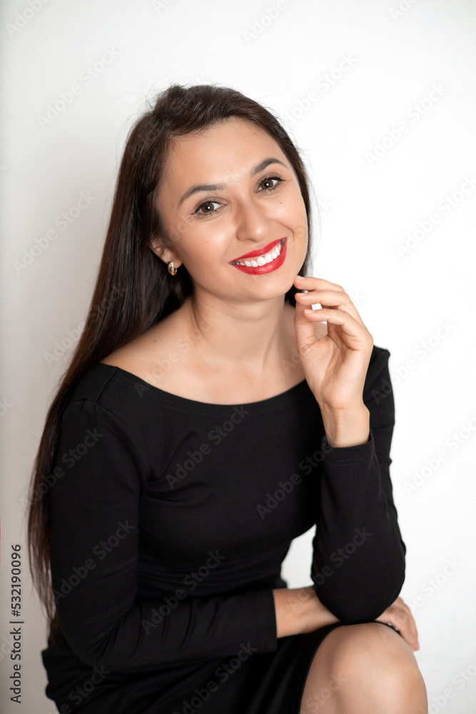 A sensual studio portrait of a beautiful young woman in a black dress with red lipstick on her lips. White background place for text A sensual studio portrait of a beautiful young woman in a black dress with red lipstick on her lips. White background place for text