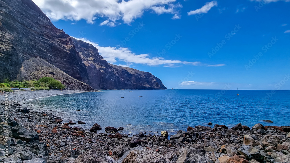 Scenic coastal hiking trail to Playas de las Arenas along massive cliffs in Valle Gran Rey on La Gomera, Canary Islands, Spain, Europe. Path leads to peak of Teguergenche. One boat in remote lagoon
