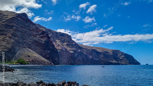 Scenic coastal hiking trail to Playas de las Arenas along massive cliffs in Valle Gran Rey on La Gomera, Canary Islands, Spain, Europe. Path leads to peak of Teguergenche. One boat in remote lagoon photo