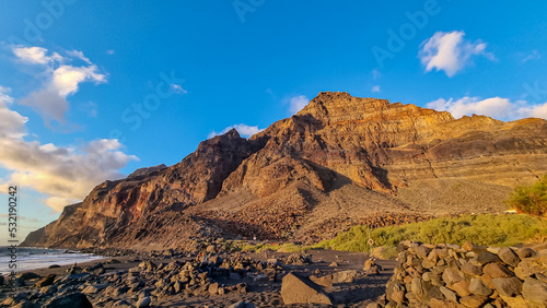 Scenic view during sunset on the volcanic sand beach Playa del Ingles in Valle Gran Rey, La Gomera, Canary Islands, Spain, Europe. Massive cliffs of the La Mercia range. Calm atmosphere at the seaside