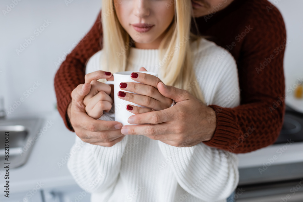 cropped view of young man hugging blonde woman with cup of tea. cropped view of young man hugging blonde woman with cup of tea.
