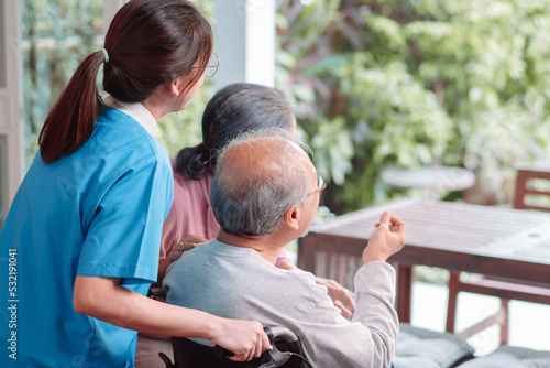 Asian caregiver nurse support senior elderly man on wheelchair in living room. nurse female take care of mature patient doing physical therapy at nursing home. Health care concept.