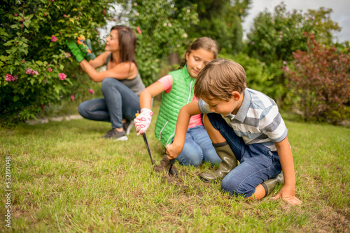 Children digging for planting while their mom take care of plants in backyard garden