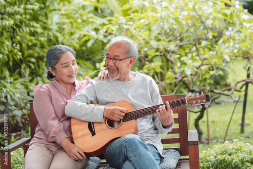 Happy Asian senior couple elderly man playing guitar music song enjoy having fun happiness outside house near backyard garden. Retirement insurance concept © Kiattisak