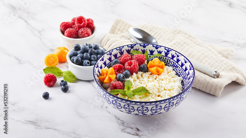 Cottage cheese in bowl garnished with raspberries, blueberries, physalis and mint leaves on white background