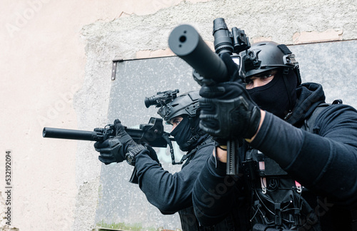 Anonymous squad fighters with rifles aiming near shabby building photo