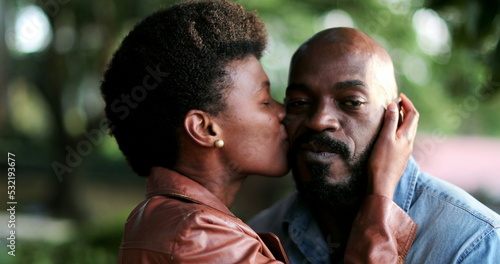 Woman kissing man in cheek, African couple romance outside at park
