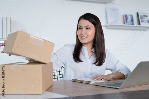 Happy young Asian woman entrepreneur, Hold package and Smile for sale success of online shopping store at home office, Concept of merchant, small business, online business and eCommerce.