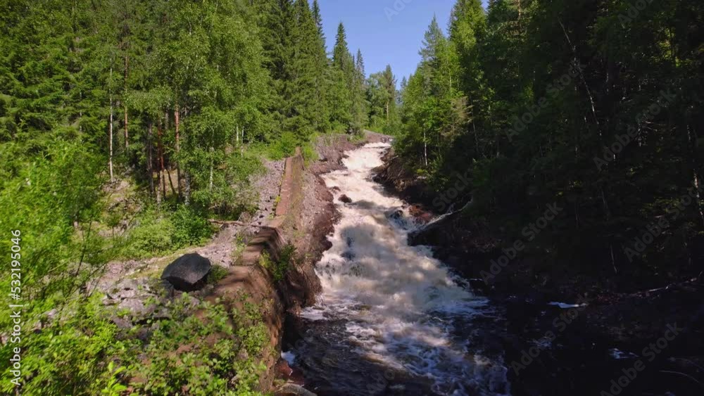 Low angle view of flowing rapids in the swedish wilderness, remains of a wall along the mountain river, rocks, pine trees and birch trees with a clear blue sky in summer. Low angle view of flowing rapids in the swedish wilderness, remains of a wall along the mountain river, rocks, pine trees and birch trees with a clear blue sky in summer.
