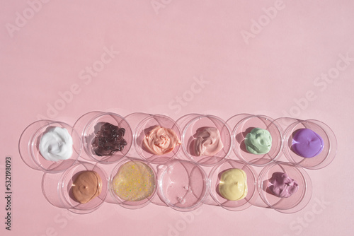 Multicolored textures of cream, scrub, serum and gel in Petri dishes on a pink background. Concept of cosmetics laboratory researches. Smear of skincare cosmetics product. Wellness and beauty concept