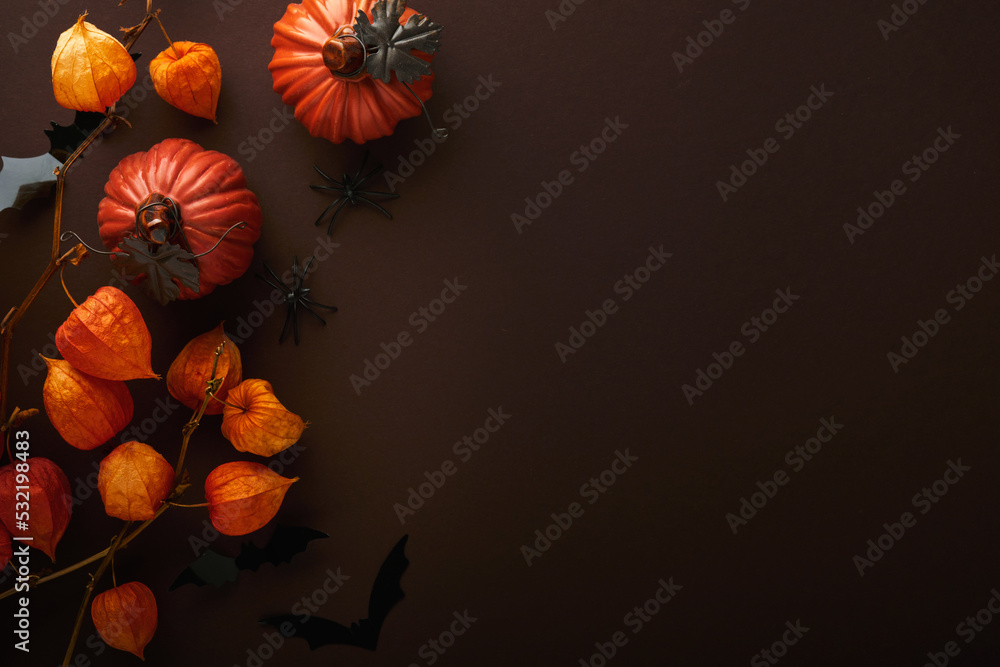 Halloween background. Flock of black bats and branch of dry orange flowers for Halloween. Black paper bat silhouettes on brown or dark background. Autumn decoration. Halloween concept. Top view.