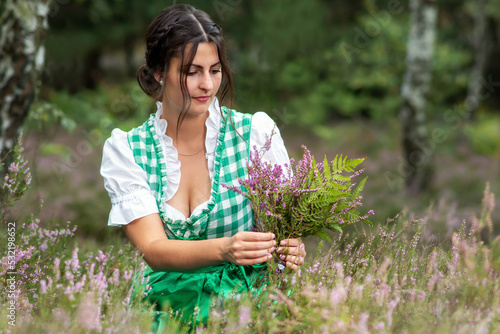 Fotografie Young woman in dirndl picks flowers in the forest