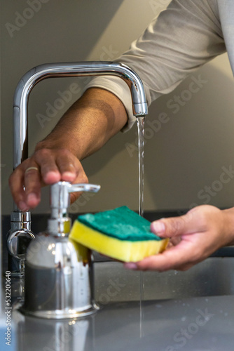Unrecognizable young man's hands with a scouring pad in the sink to clean dishes