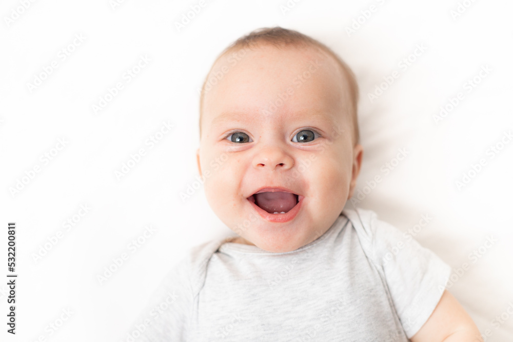 The baby lies on a white background and smiles at the camera . Advertising of children's goods. A child on a white background. Happy baby. The smile of a child. Children 's article .