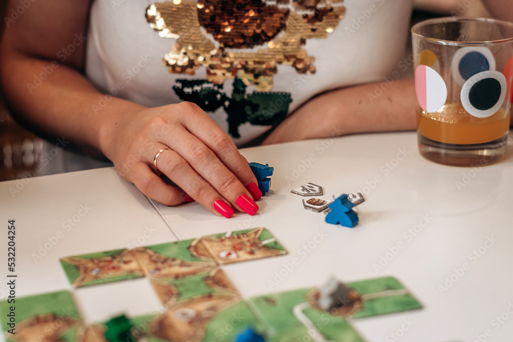 A group of young people play board games at home in the kitchen.Women's hands close-up.Time together.Stay home,board games concept.Selective focus. A group of young people play board games at home in the kitchen.Women's hands close-up.Time together.Stay home,board games concept.Selective focus.