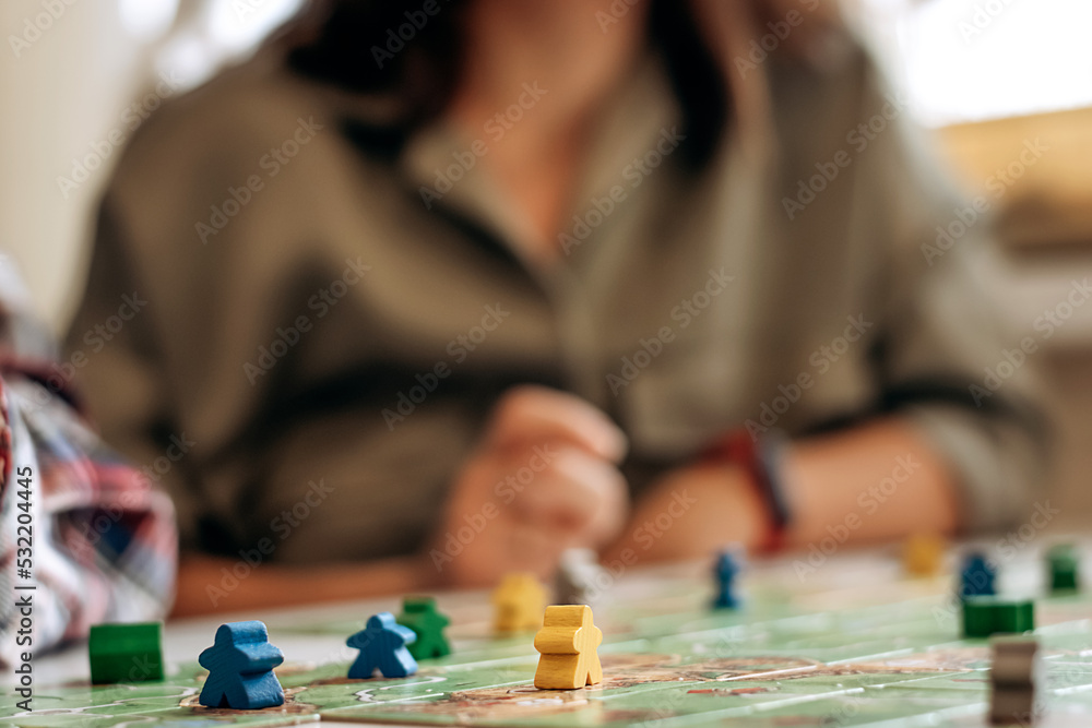 Field of tabletop game with gaming pieces in focus and blurred players on the background.Time together.Stay home,board games concept.Selective focus,close up. Field of tabletop game with gaming pieces in focus and blurred players on the background.Time together.Stay home,board games concept.Selective focus,close up.