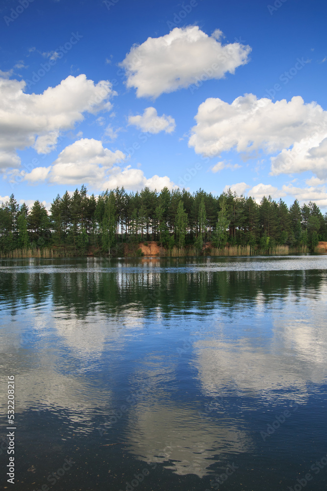 Summer landscape in the lake water reflects the forest and the sky with clouds.