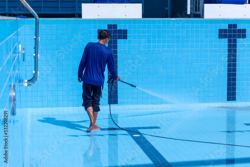 Swimming Pool Cleaning., A service man is cleaning the pool ground with a pressure pump