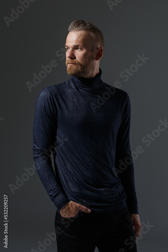 Portrait of a handsome bearded man in black clothes isolated on a dark background.