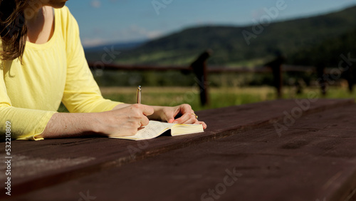 Fototapeta Naklejka Na Ścianę i Meble -  Woman writing in paper notebook journal in nature mountains landscape. Travel journaling concept.
