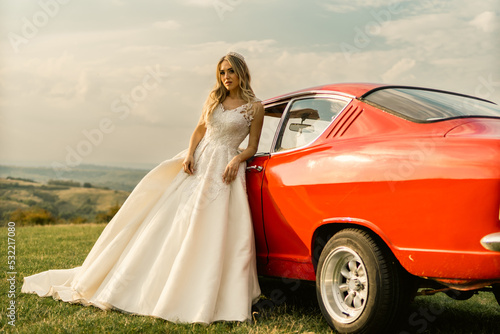 Beautiful bride posing with old vintage red car in sunset. © DusanJelicic