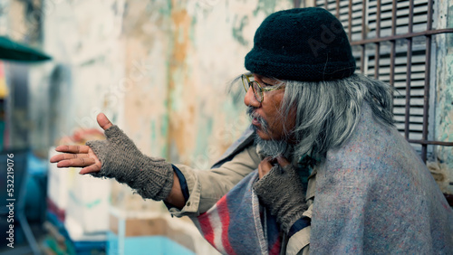  Close-up of a long-haired, dressed Asian man sitting on a wall in an alley, waiting for money and food from passers-by waiting for help. Homeless people who do not have home to sleep on streets photo