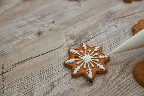 Close up of drawing gingerbread Christmas snowflake sugar cookie on wooden table background with white icing