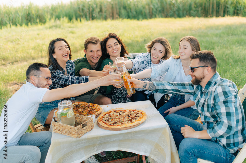 Group of friends are relaxing together outdoor. Young cheerful people clink glasses and laugh.