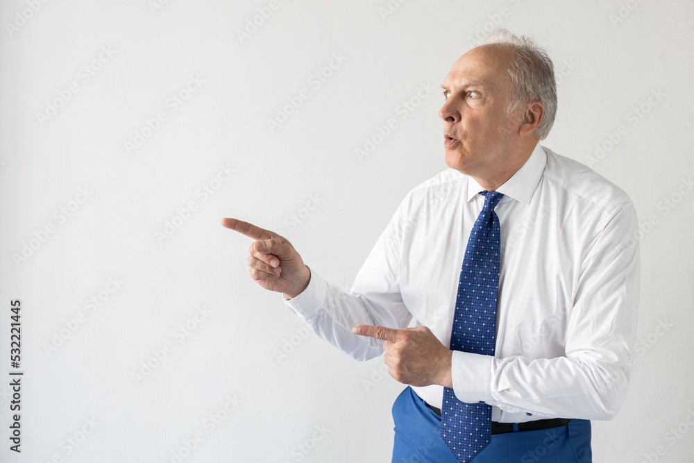 Portrait of shocked mature businessman pointing at something. Senior man wearing formalwear showing something in surprise. Advertising and presentation concept Portrait of shocked mature businessman pointing at something. Senior man wearing formalwear showing something in surprise. Advertising and presentation concept